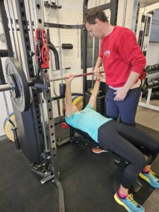 Participant pressing a weight up from their chest to straight arms, with support from researcher