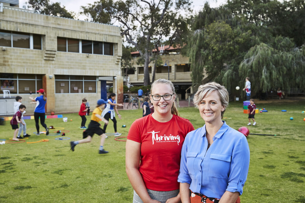 Thriving founder Bonnie Furzer and staff member smiling at the camera. They are standing in front of a green outdoor space, with kids running around in the background.