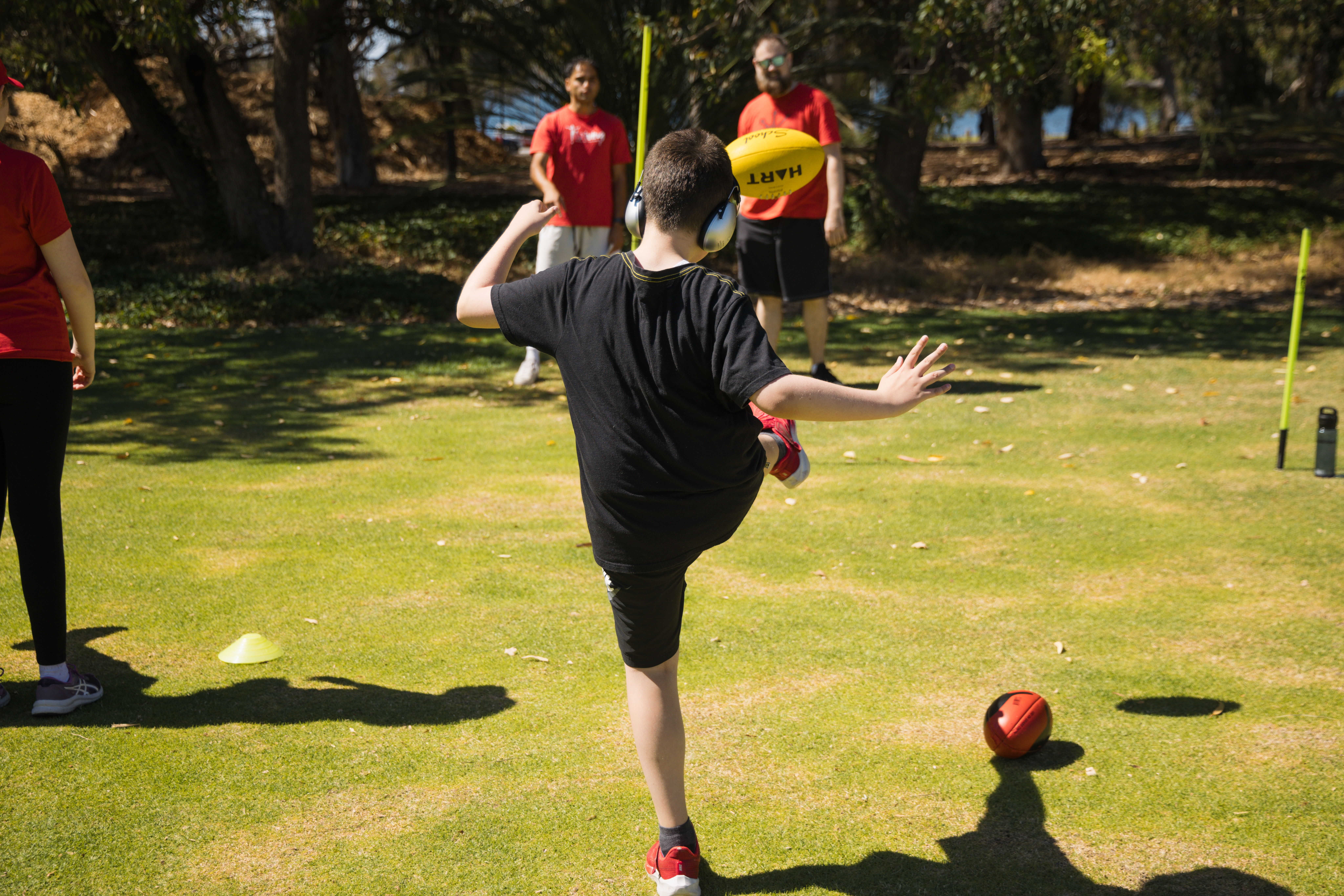 Youn person wearing noise cancelling earphones kicking an aussie football
