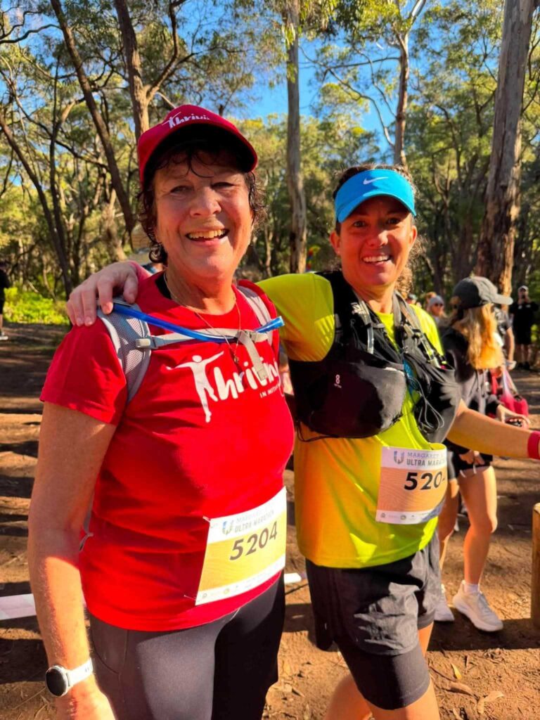 Two smiling women wearing race bibs at the Margaret River Ultra Marathon, one in a red Thriving in Motion shirt.
