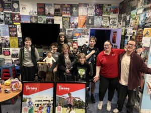A group of young people and Thriving in Motion staff smiling and laughing together in a community youth space