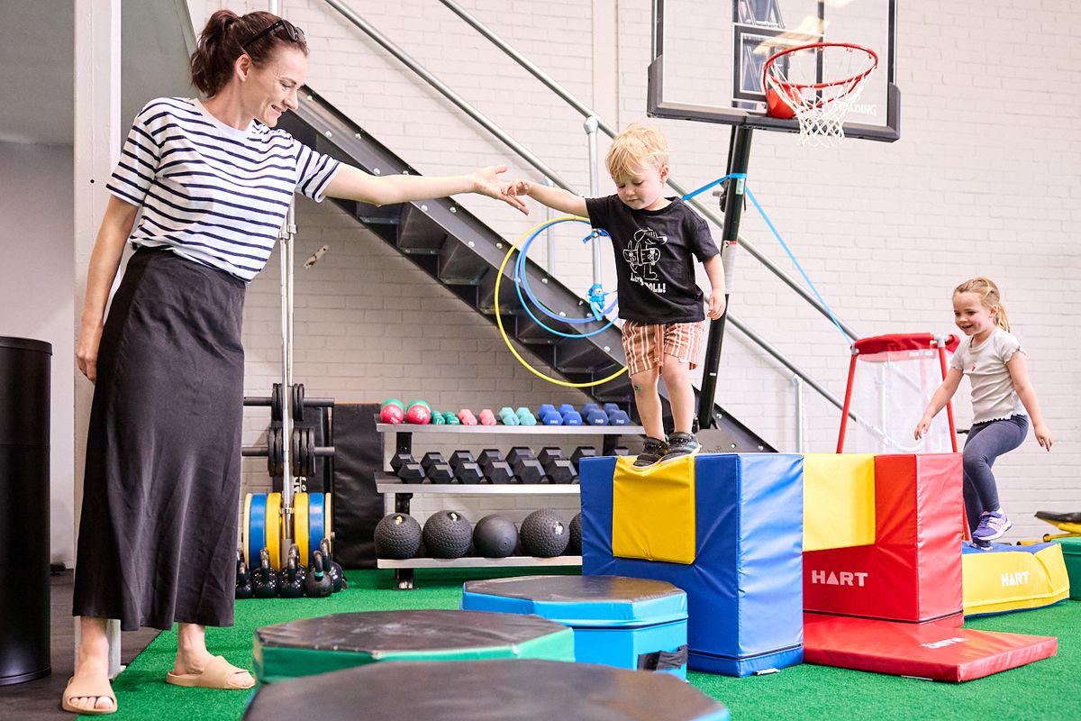 A mum holding her son's hand as he jumps off a soft block at Mini Movers in Balcatta