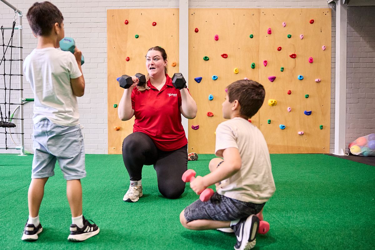 A Thriving in Motion team member coaching two boys with dumbbells in the strength area
