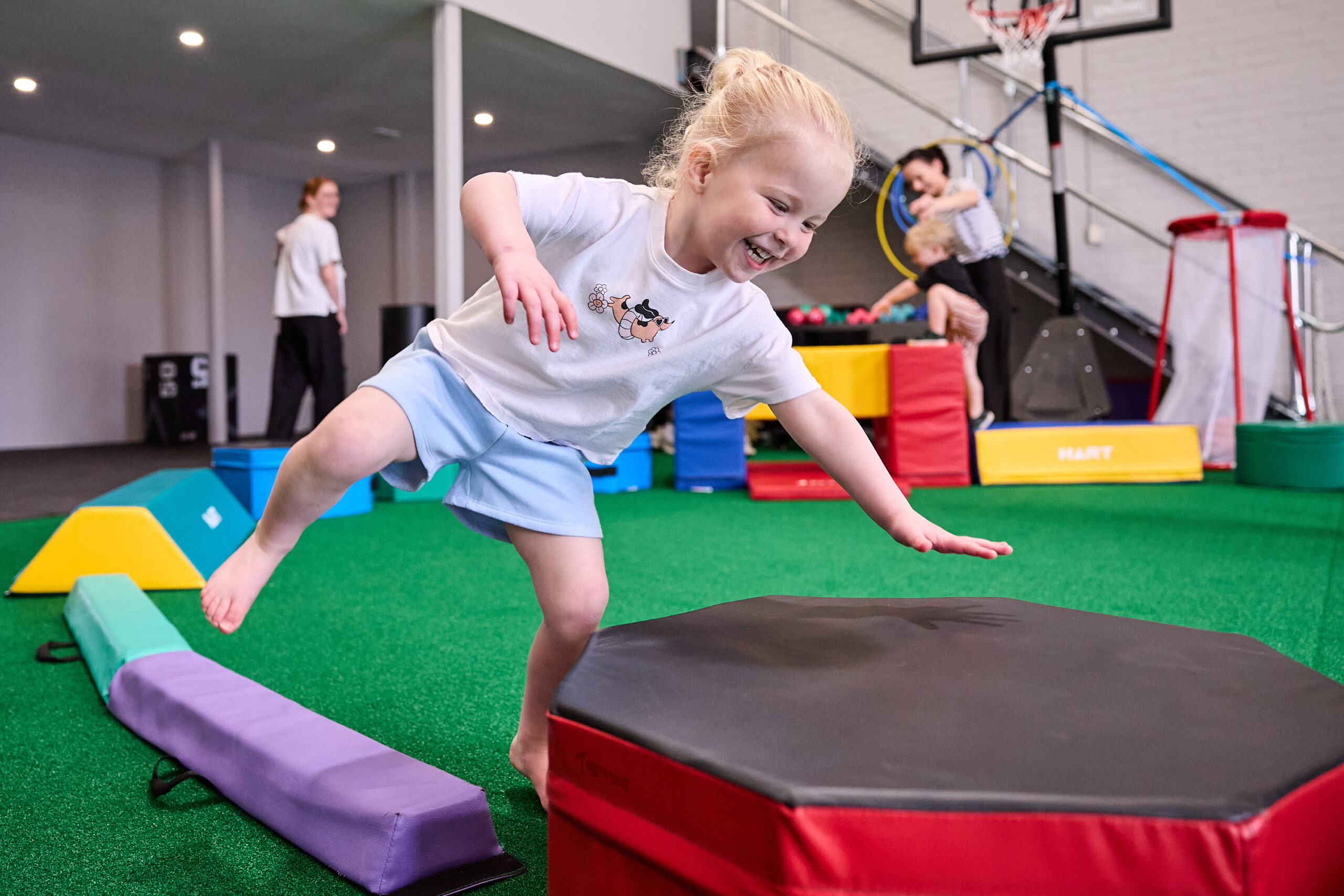 A young girl jumping off a soft play platform in the open exercise space at Thriving HQ, Balcatta