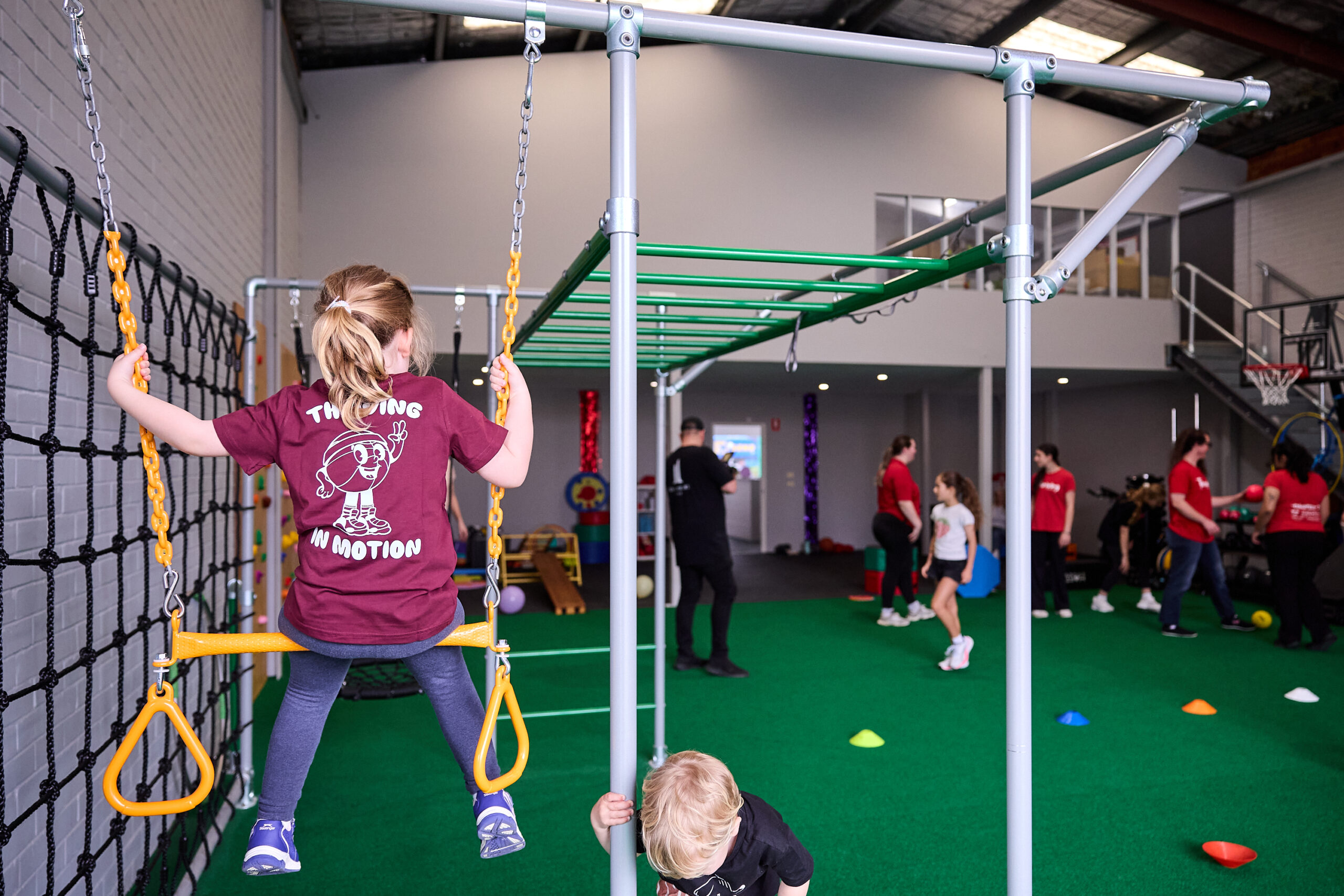 A child on a swing in the open exercise space at Thriving HQ, seen from behind
